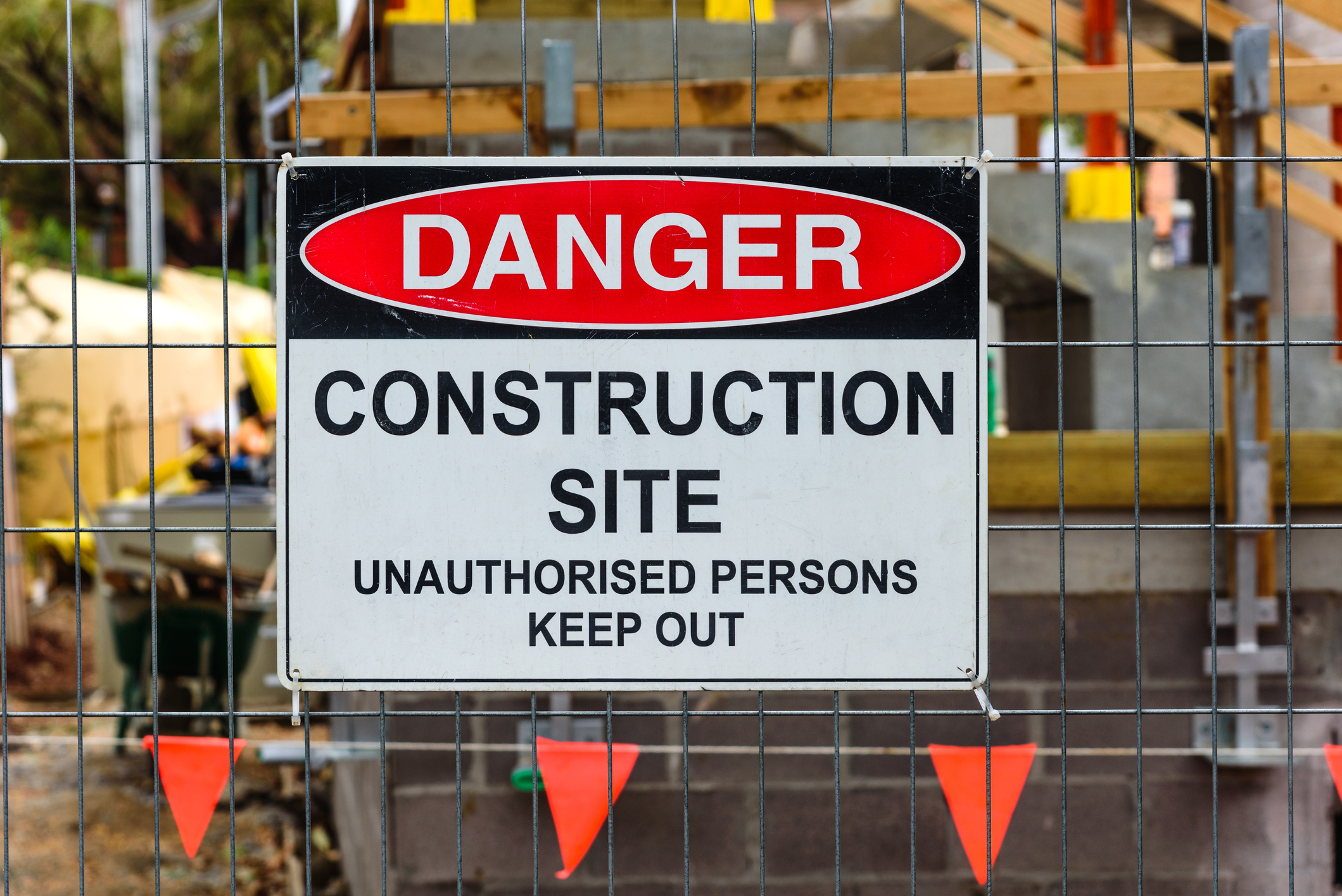 A 'Danger, Construction site, Unauthorised Persons Keep Out' sign mounted on a wire fence in front of a building site